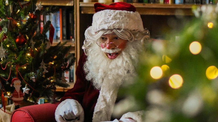 Head and shoulder of Father Christmas telling a story surrounded by lights and festive decorations